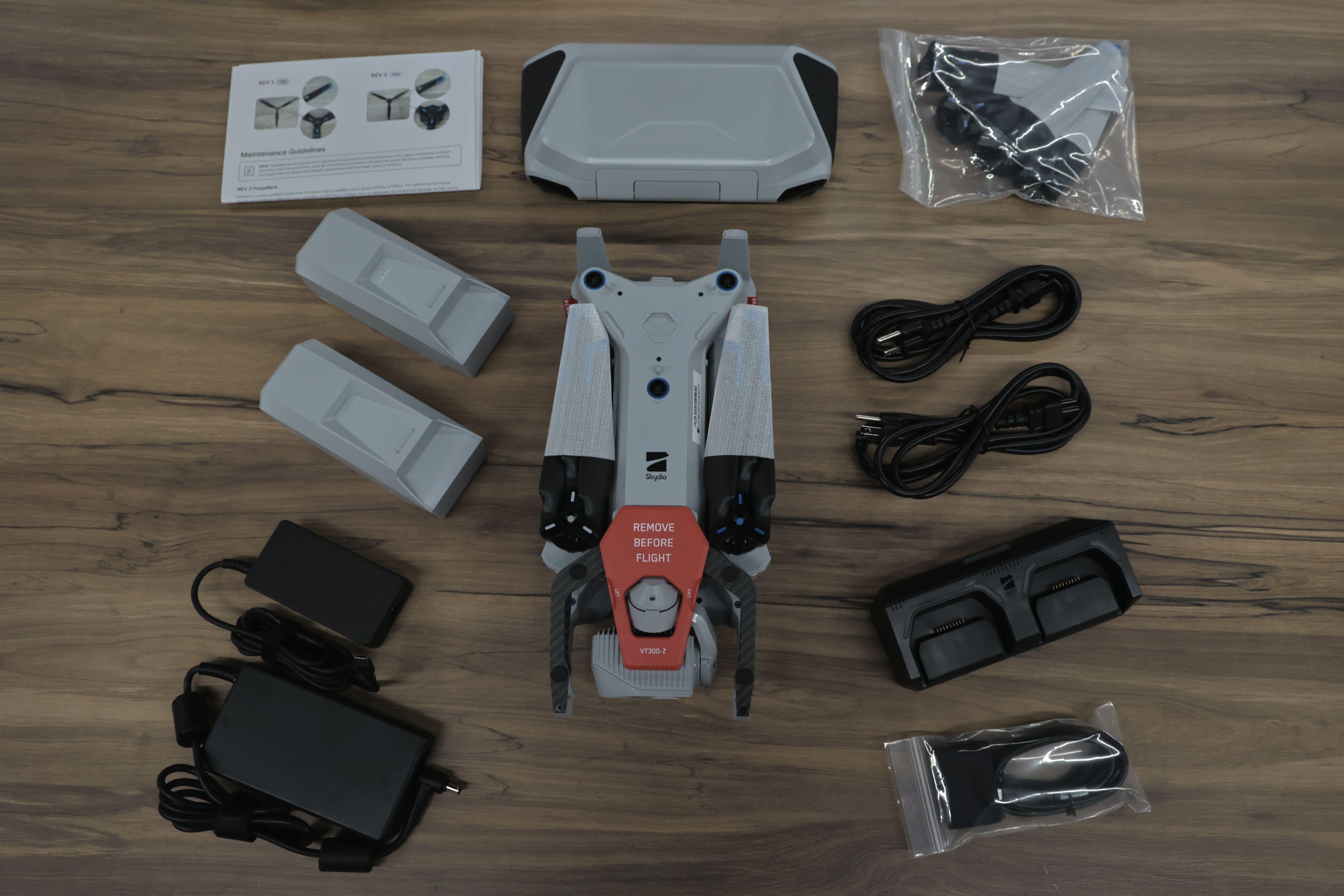 Skydio X10 無人機完整套件平放展示，包含無人機本體、兩顆電池、雙電池充電座、變壓器與電源線、攜行收納盒、配件與維護說明文件，整齊排列於木質桌面上。