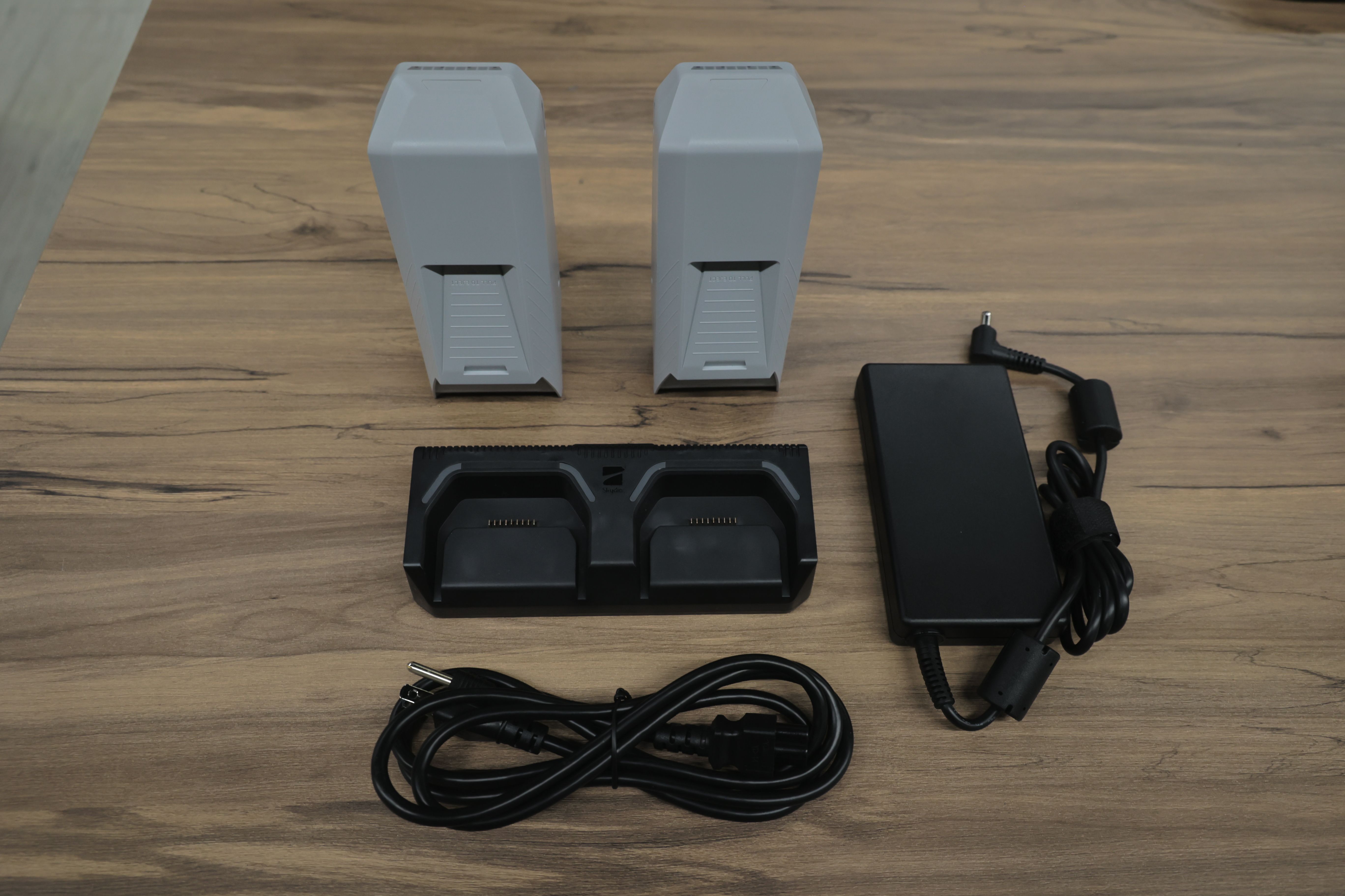 兩顆 Skydio 無人機電池、雙電池充電座、電源變壓器與電源線平放展示於木質桌面上，所有配件整齊排列，呈現充電與電力管理相關組件配置。