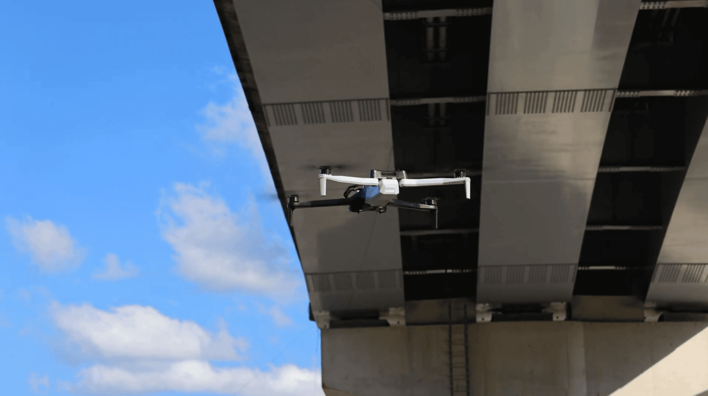 一架多旋翼無人機 Skydio X10 在橋梁下方結構空間飛行,背景可見橋面結構與天空,呈現無人機於橋梁巡檢作業中的應用情境。